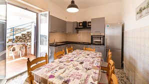 A compact kitchen with grey cabinets, a stainless steel refrigerator, and a dining table with a floral tablecloth. - Casa Fetovaia (Campo nell'Elba)