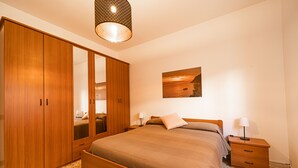 A bedroom with a wooden bed, a large wardrobe, a nightstand with a lamp, and a painting on the wall. - Casa Fetovaia (Campo nell'Elba)
