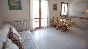 A room with a bed, a dining table with chairs, a kitchen area, and a large window with curtains. - Appartamenti Rosa (Campo nell'Elba)