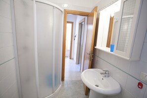Un bagno con cabina doccia in vetro, un lavandino bianco e uno specchio sopra.