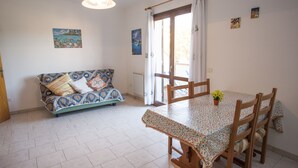 A dining area with a table and chairs, a sofa with patterned cushions, a hanging light fixture, and artwork on the walls. - Appartamenti Rosa (Campo nell'Elba)