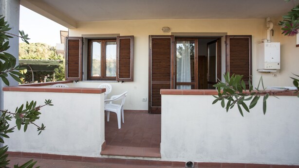 A covered outdoor area with a table and chairs, wooden shutters, and a white wall. - Appartamenti Rosa (Campo nell'Elba)