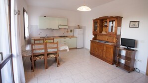 A kitchen with a dining table, chairs, a refrigerator, wooden cabinets, and a television. - Appartamenti Rosa (Campo nell'Elba)