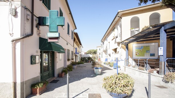 Une rue étroite, bordée de bâtiments des deux côtés, avec une pharmacie et un panneau indiquant les directions.