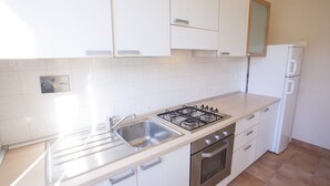 Une cuisine avec des meubles blancs, un évier en acier inoxydable, une cuisinière à gaz et un réfrigérateur blanc.