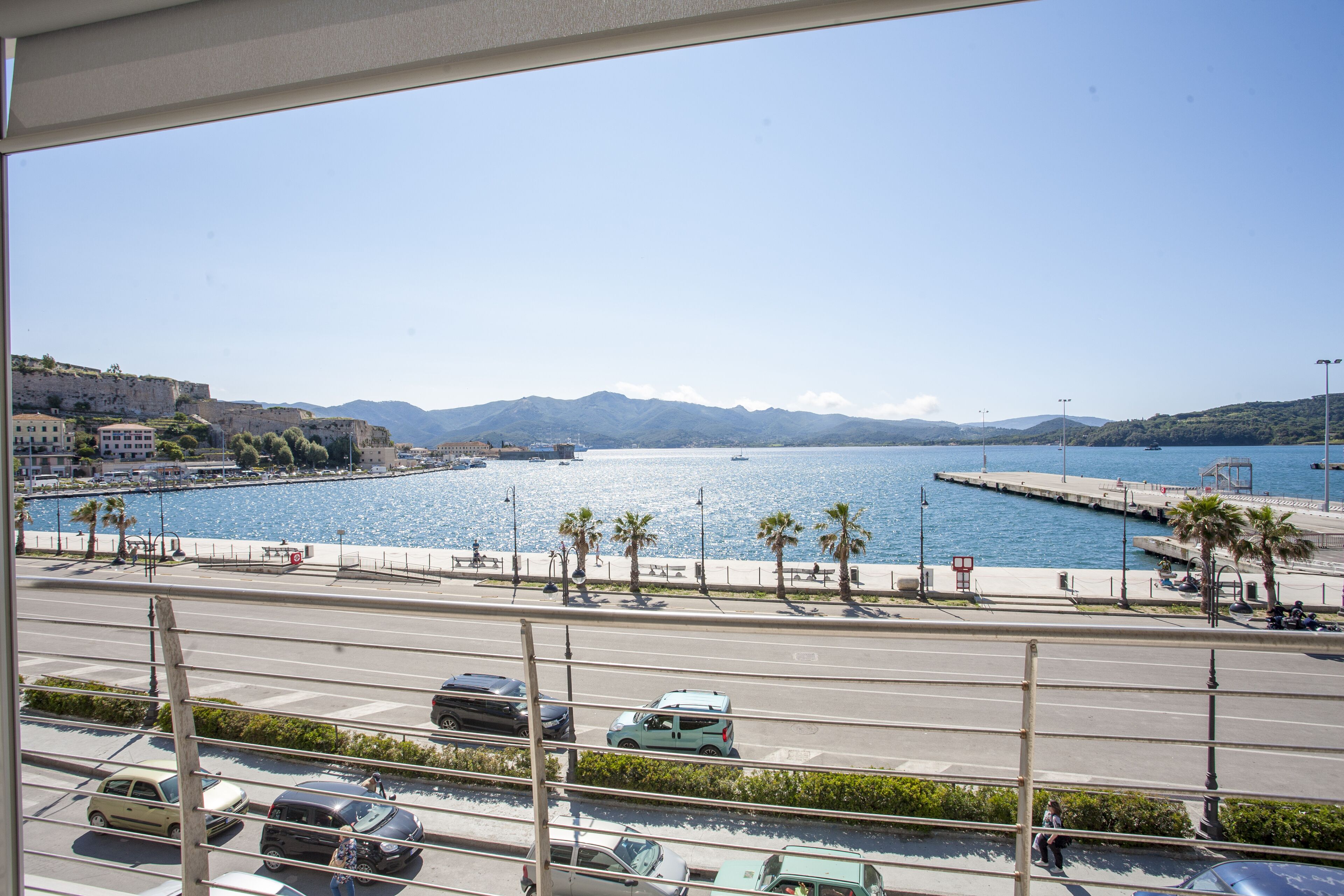 A coastal cityscape with a marina, parked cars, and a clear sky.