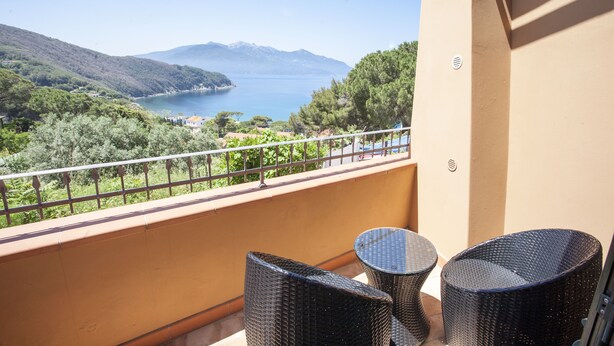 A balcony with wicker furniture overlooking a scenic view of a lake and mountains. - Bilocale Paradiso (Portoferraio)