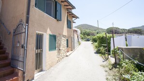 A narrow street with a building featuring stone walls and green shutters. - Bilocale Paradiso (Portoferraio)