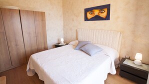 A bedroom with a large bed, a nightstand, a wardrobe, and a painting on the wall. - Bilocale Paradiso (Portoferraio)