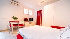 A bedroom with a bed, a desk, a chair, a television, and a red door. - Monolocale Nanni (Portoferraio)