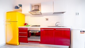 A kitchen with a yellow refrigerator, red cabinets, a white sink, and a small stove. - Monolocale Nanni (Portoferraio)