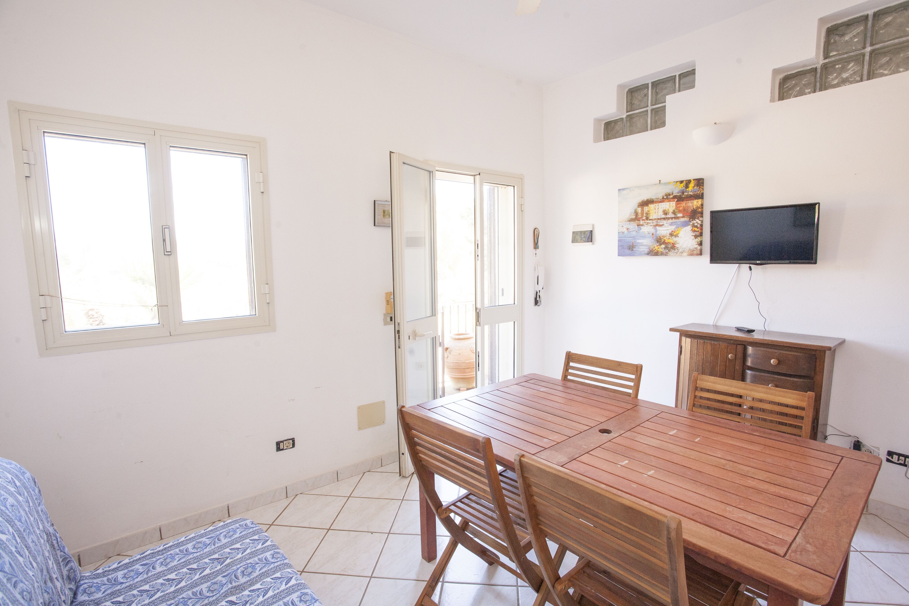 Un comedor con una mesa y sillas de madera, un televisor montado en la pared y una ventana con persianas.