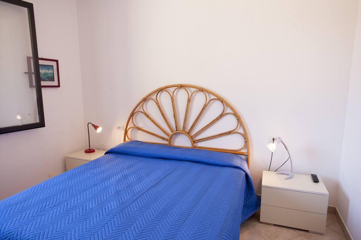 Quarto com uma cama, duas mesas de cabeceira e duas luminárias.