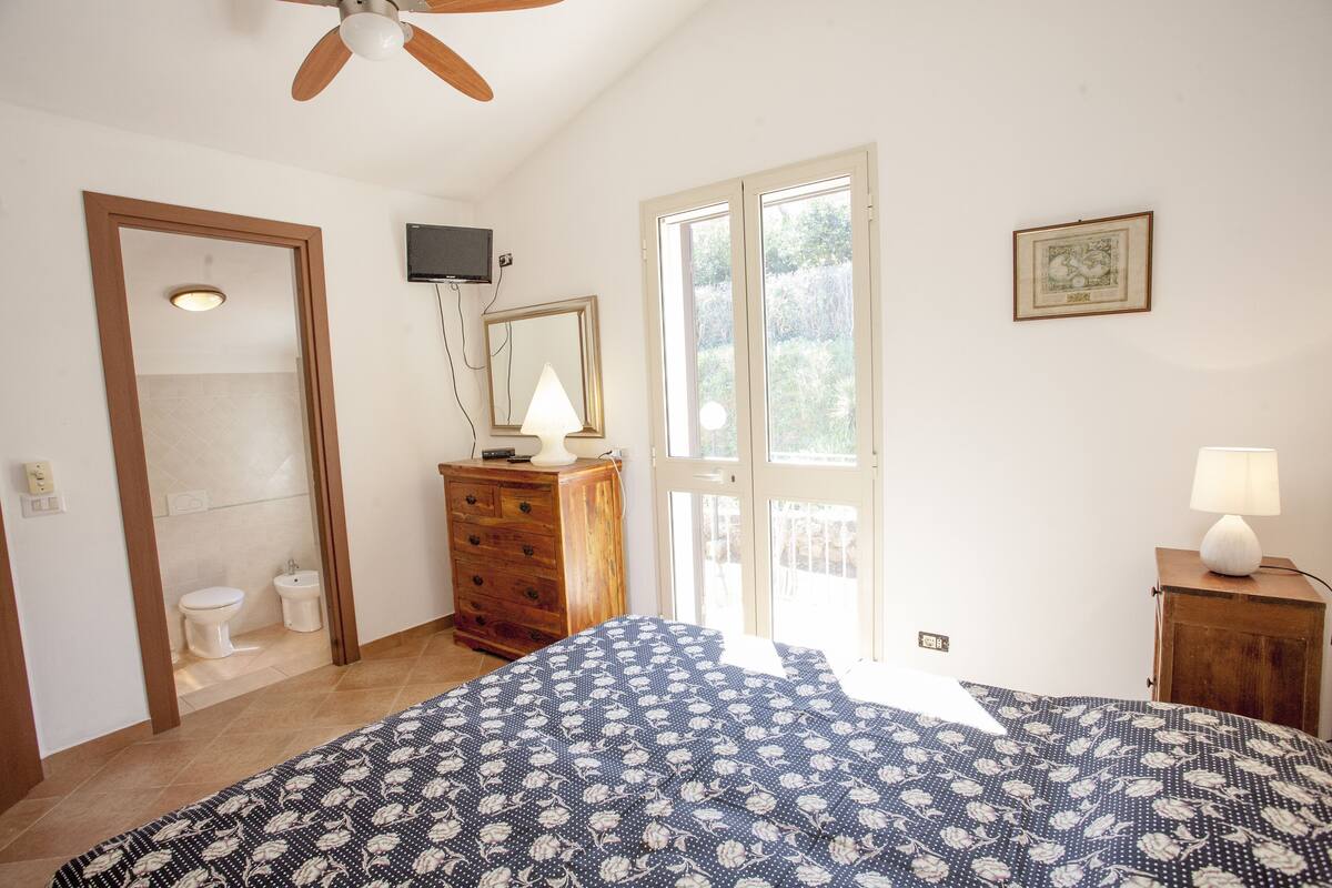 Quarto com cama, penteadeira, televisão e janela.
