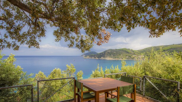 A terrace with a wooden table and chairs, overlooking a scenic coastal view with hills and the sea. - Villa Il Leccio sul Mare (Portoferraio)