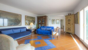 A spacious living room with a blue sofa, a wooden cabinet, and a tiled floor. - Villa Il Leccio sul Mare (Portoferraio)
