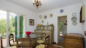 A dining area with a glass table surrounded by wooden chairs, a wooden cabinet with decorative plates, and a chandelier. - Villa Il Leccio sul Mare (Portoferraio)