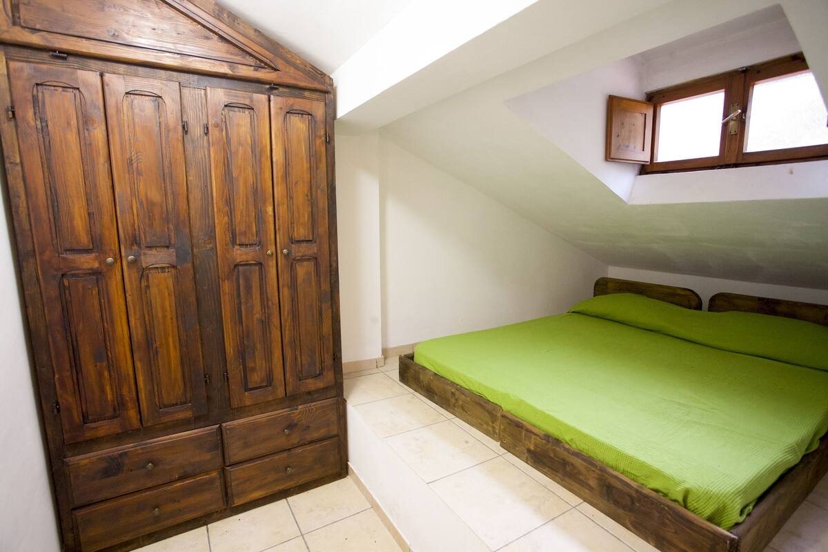 A bedroom with a wooden wardrobe, a green bed, and a skylight.