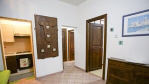 A hallway with a kitchen area on the left, a wooden door with a mirror, and a framed picture on the wall. - Appartamenti Home 75 (Portoferraio)