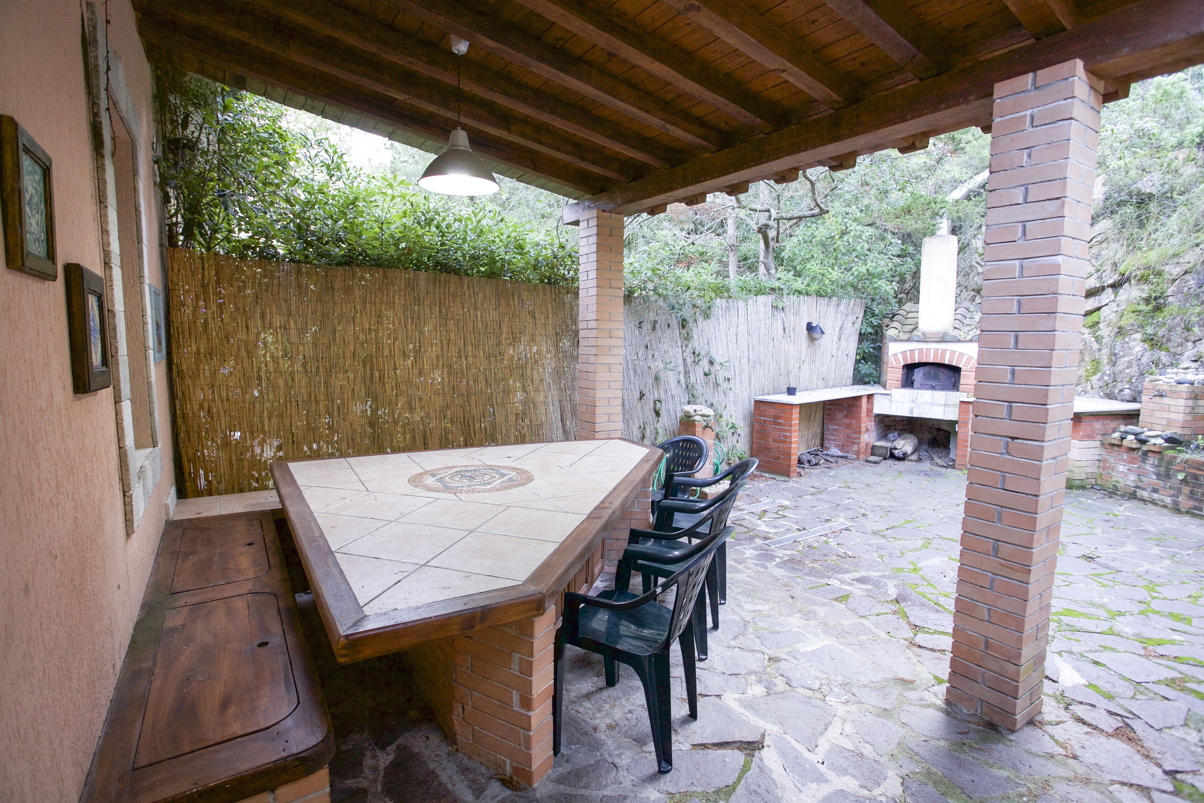An outdoor patio with a brick table and chairs, a hanging light fixture, and a brick chimney in the background.