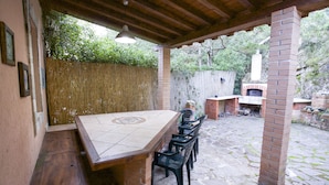 An outdoor patio with a brick table and chairs, a hanging light fixture, and a brick chimney in the background. - Appartamenti Home 75 (Portoferraio)