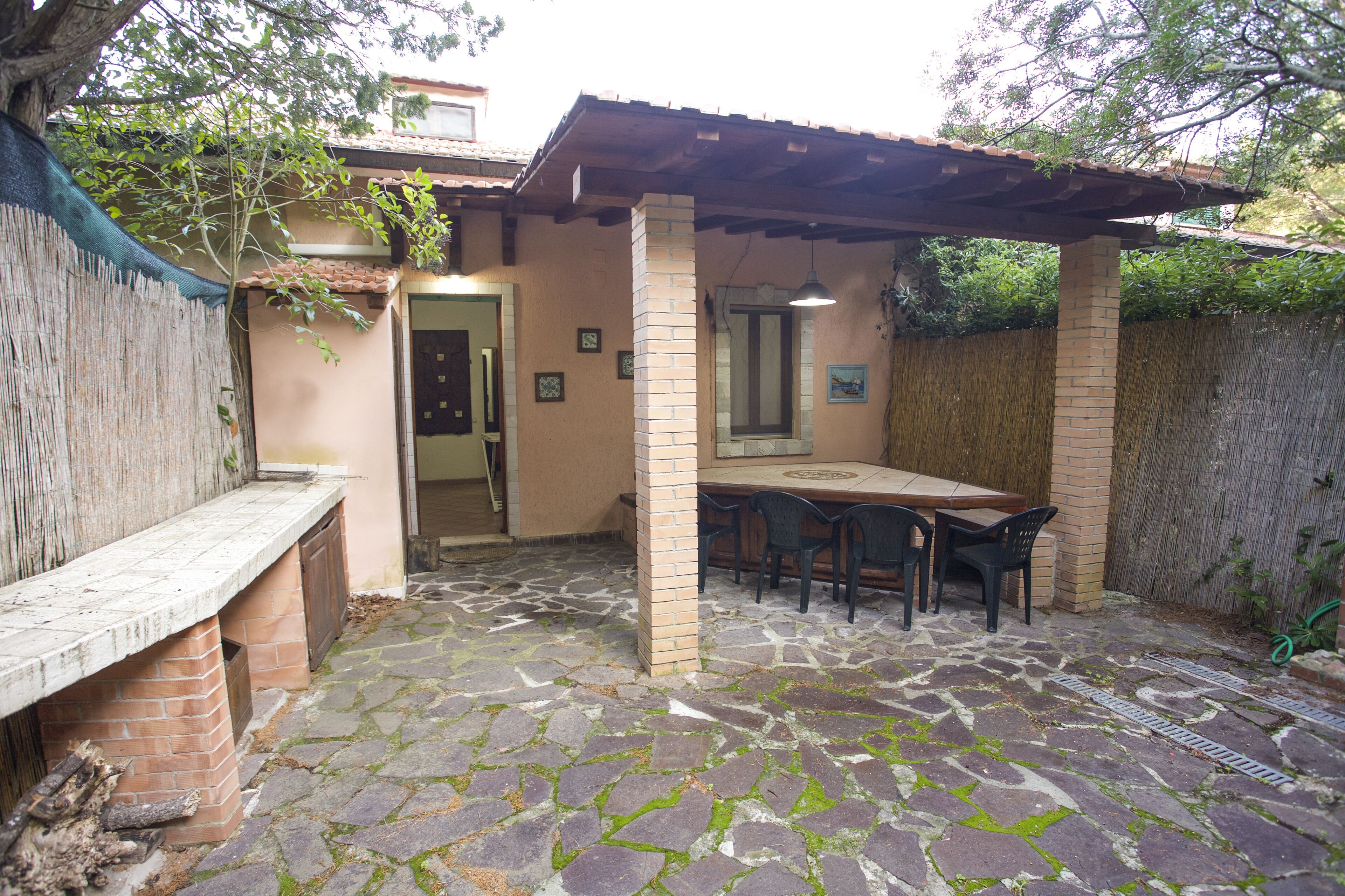 Een terras met een stenen vloer, een houten bank, een tafel met stoelen en een pergola.