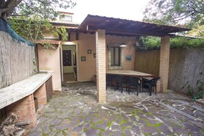 A patio with a stone floor, a wooden bench, a table with chairs, and a pergola structure. - Appartamenti Home 75 (Portoferraio)
