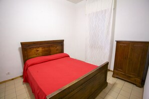A single bed with a wooden headboard and a red bedspread in a room with white walls and a tiled floor. - Appartamenti Home 75 (Portoferraio)