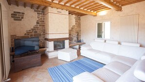 A living room with a stone fireplace, a television, and a white sofa. - Villetta Paradiso (Portoferraio)