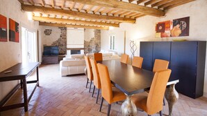 A dining area with a wooden table and orange chairs, a stone wall, and a television in the background. - Villetta Paradiso (Portoferraio)