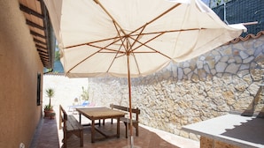 A patio area with a wooden table and chairs, a large umbrella, and a stone wall. - Villetta Paradiso (Portoferraio)