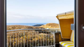 A balcony with a yellow chair, a metal railing, and a view of the sea and hills.