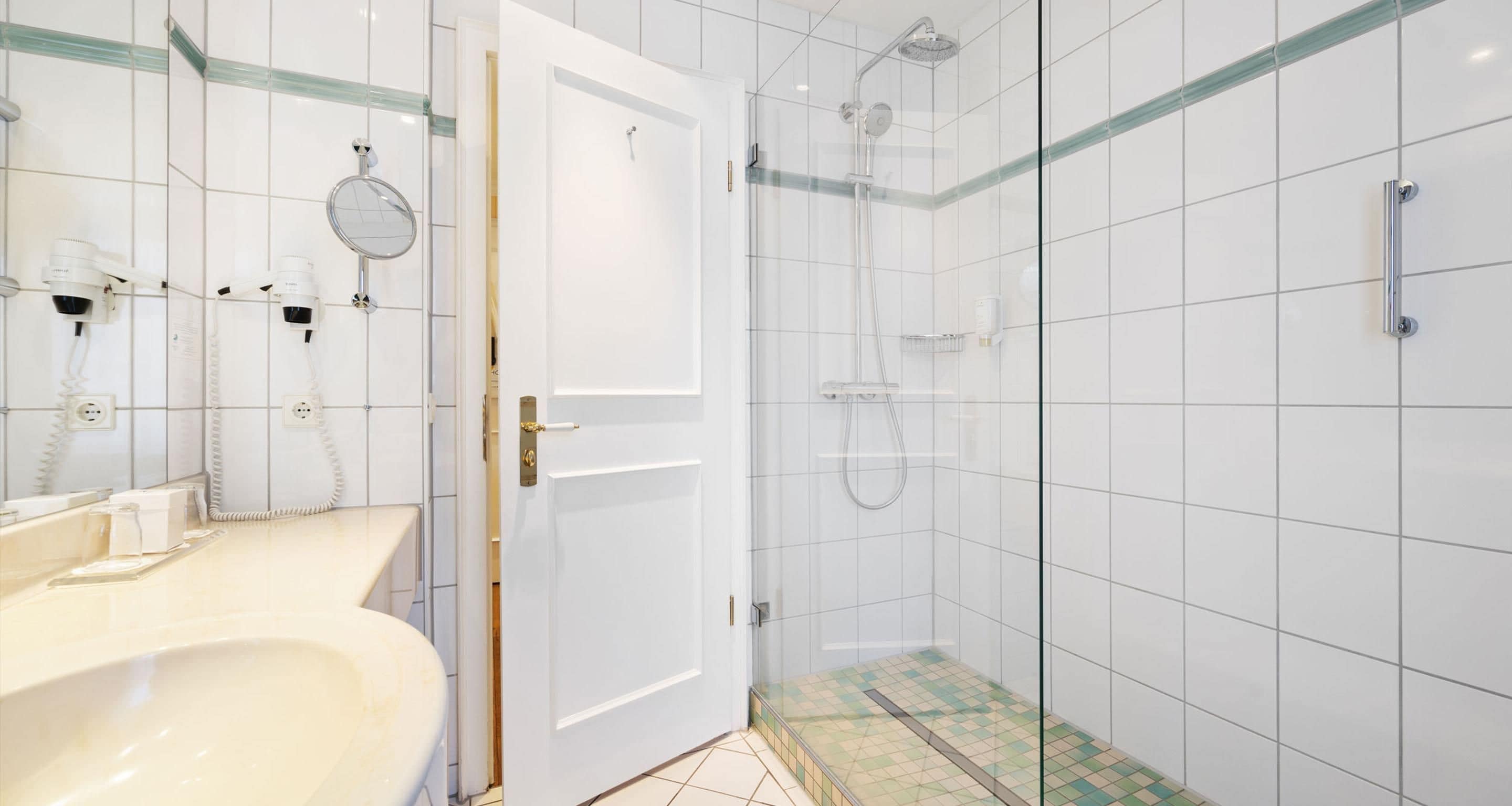 A bathroom with a white sink, a mirror, a glass shower enclosure, and a tiled floor.