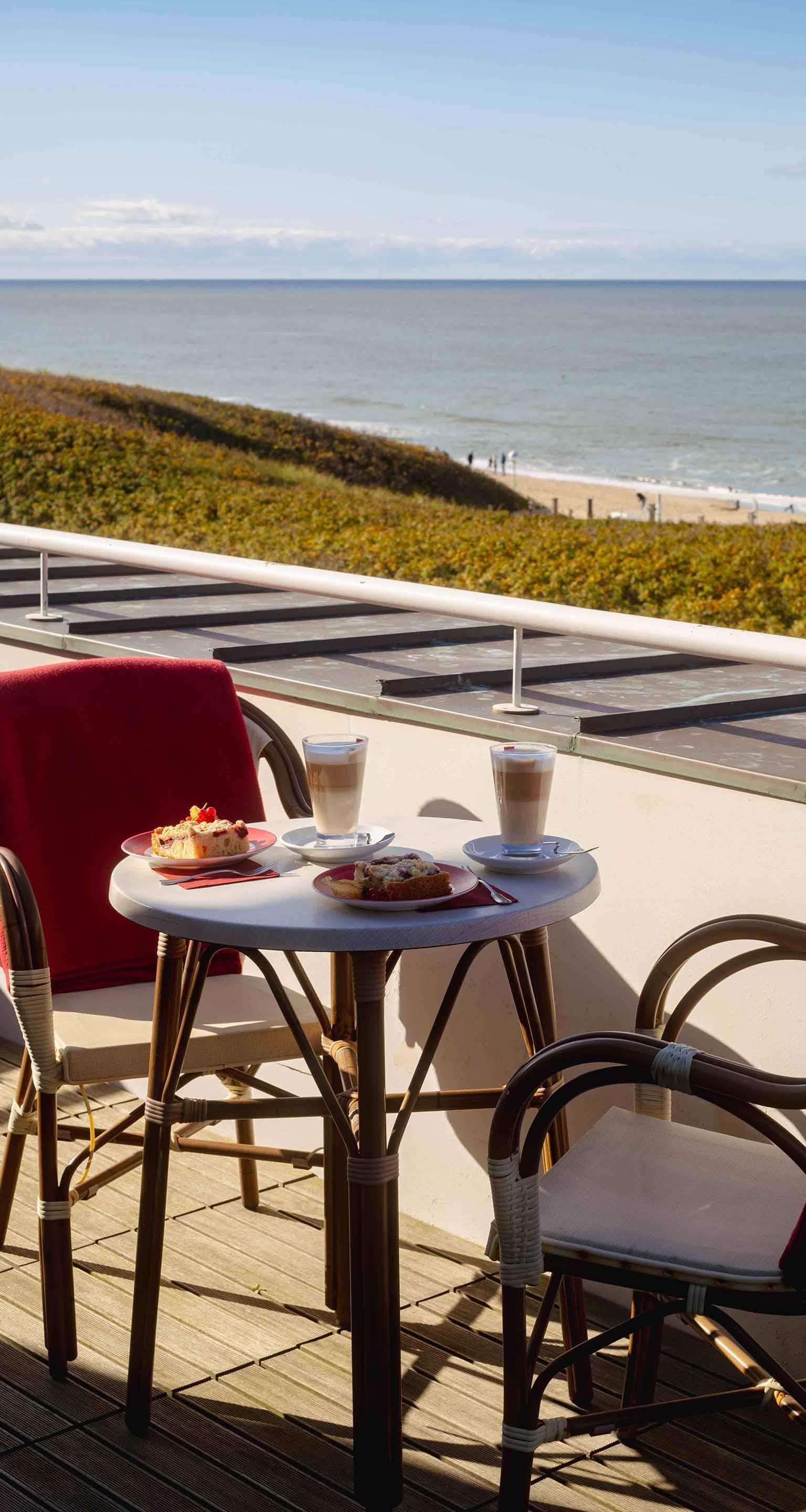 Eine Strandterrasse mit Tischen, Stühlen und Blick auf das Meer.