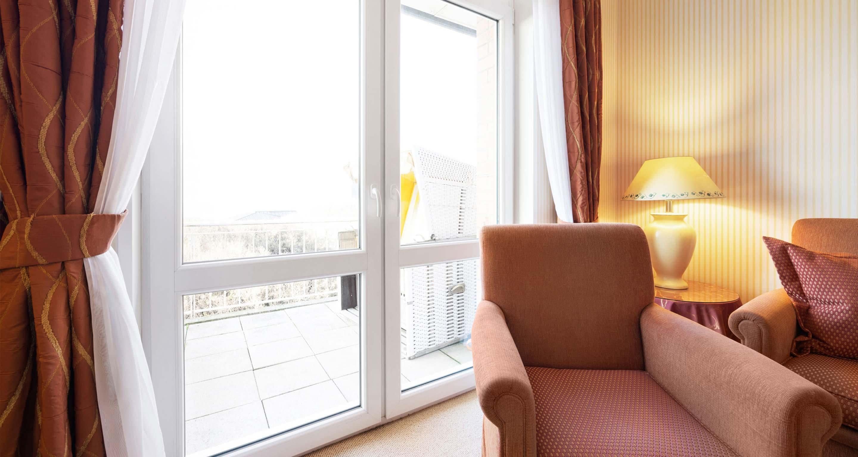 Ein Zimmer mit großem Fenster, einem Sessel, einer Lampe und Blick ins Freie.