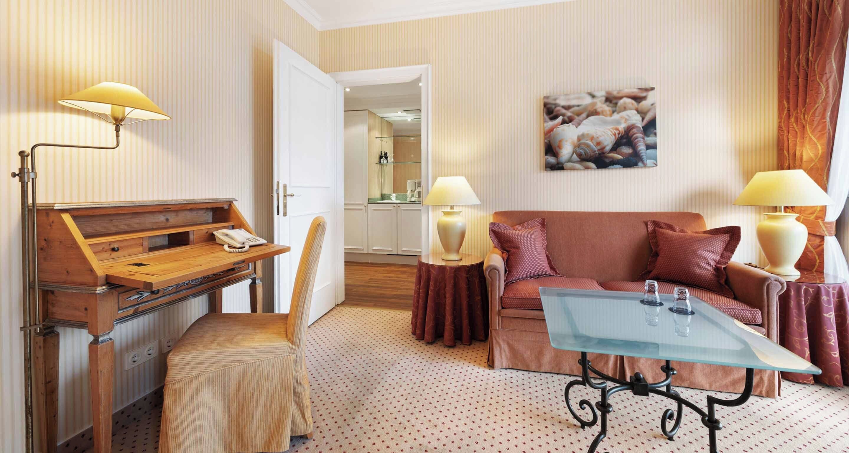 Une chambre d’hôtel avec un bureau en bois, une table basse en verre, un canapé et un fauteuil.