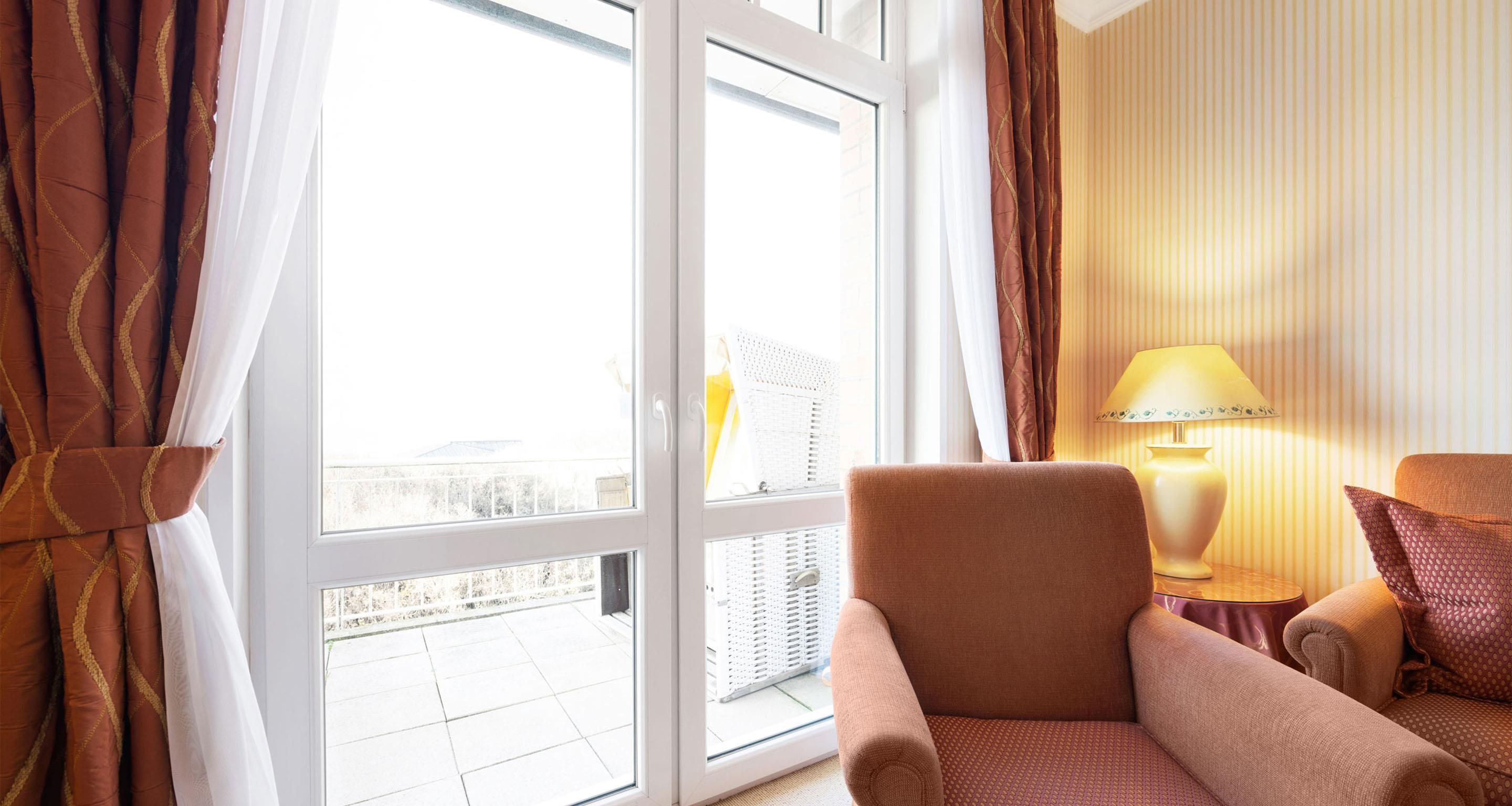 Een hotelkamer met een groot raam, een stoel, een lamp en uitzicht op het omliggende landschap.