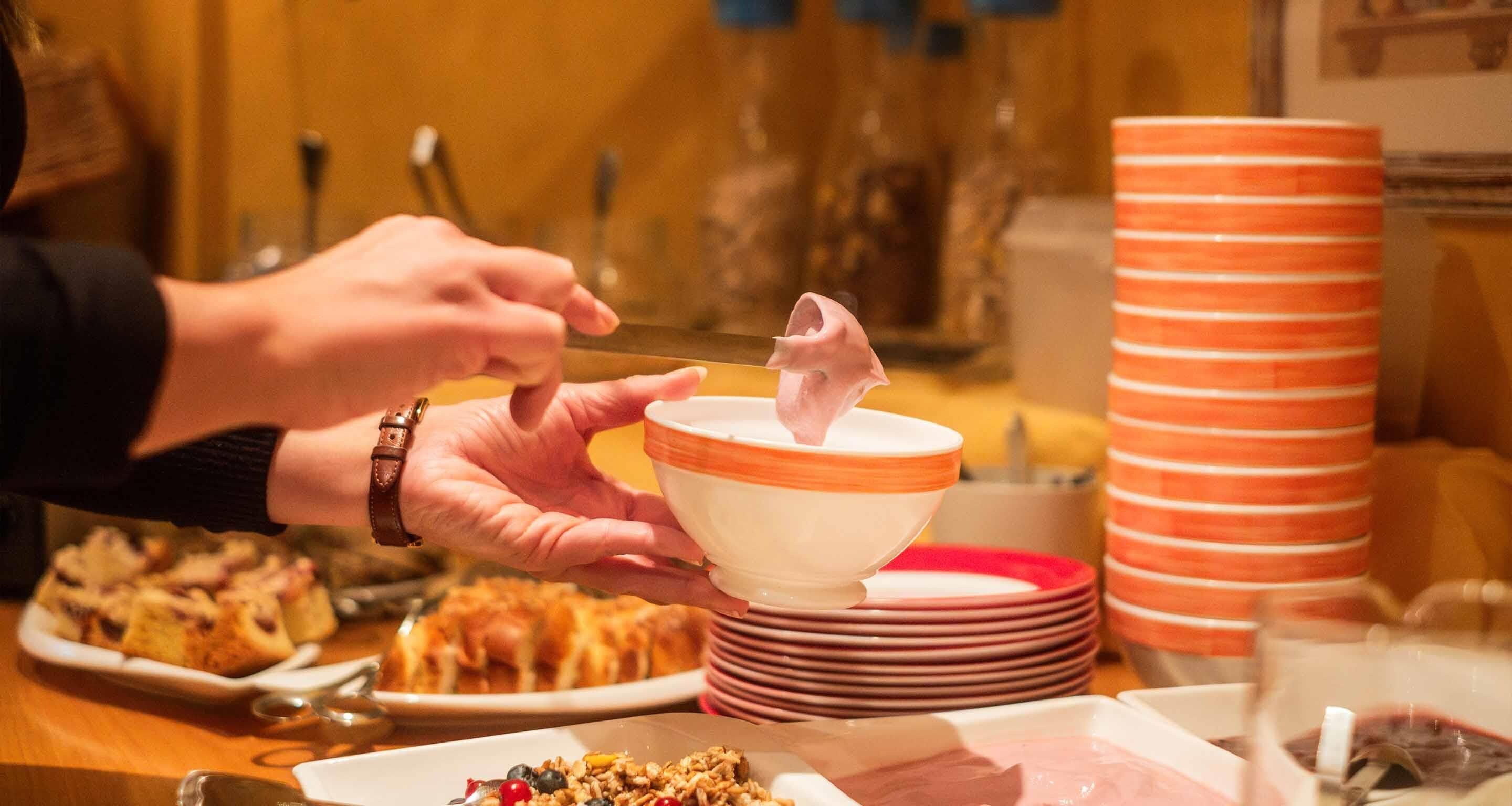 A person holding a bowl with a pink substance, possibly food, with plates and bowls in the background.