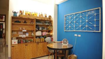 A room with a blue wall, a wooden cabinet with various items, a round table with chairs, and a fan.