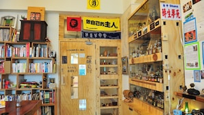 Een kamer met houten planken vol boeken en diverse spullen. Er staat een houten kast met glazen deuren waar meer spullen in staan. Een bord met Japanse tekens hangt aan de muur.