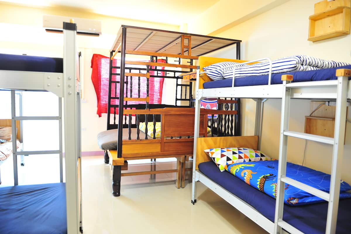 A dormitory room with bunk beds, a wooden ladder, and a window.