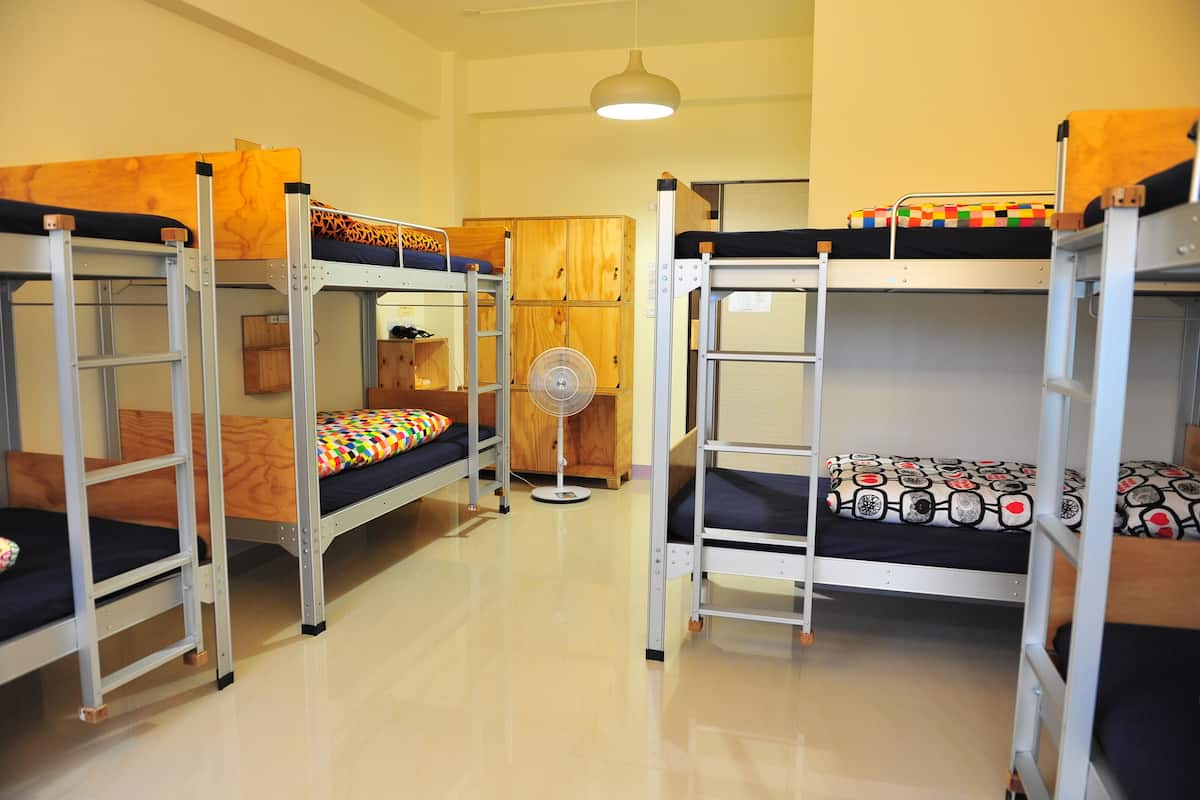 A dormitory room with bunk beds, a fan, and wooden cabinets.