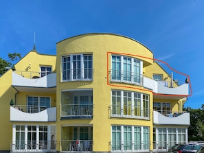 A yellow multi-story building with balconies, large windows, and a curved facade.