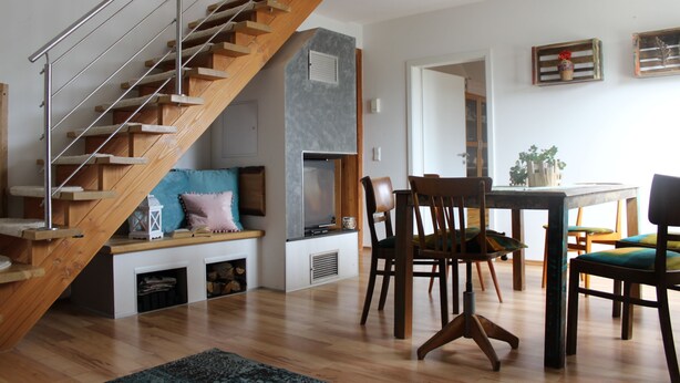 A modern living room with a wooden staircase, a dining area with wooden chairs, and a built-in entertainment unit. - Vacation on the pony farm (Priborn)
