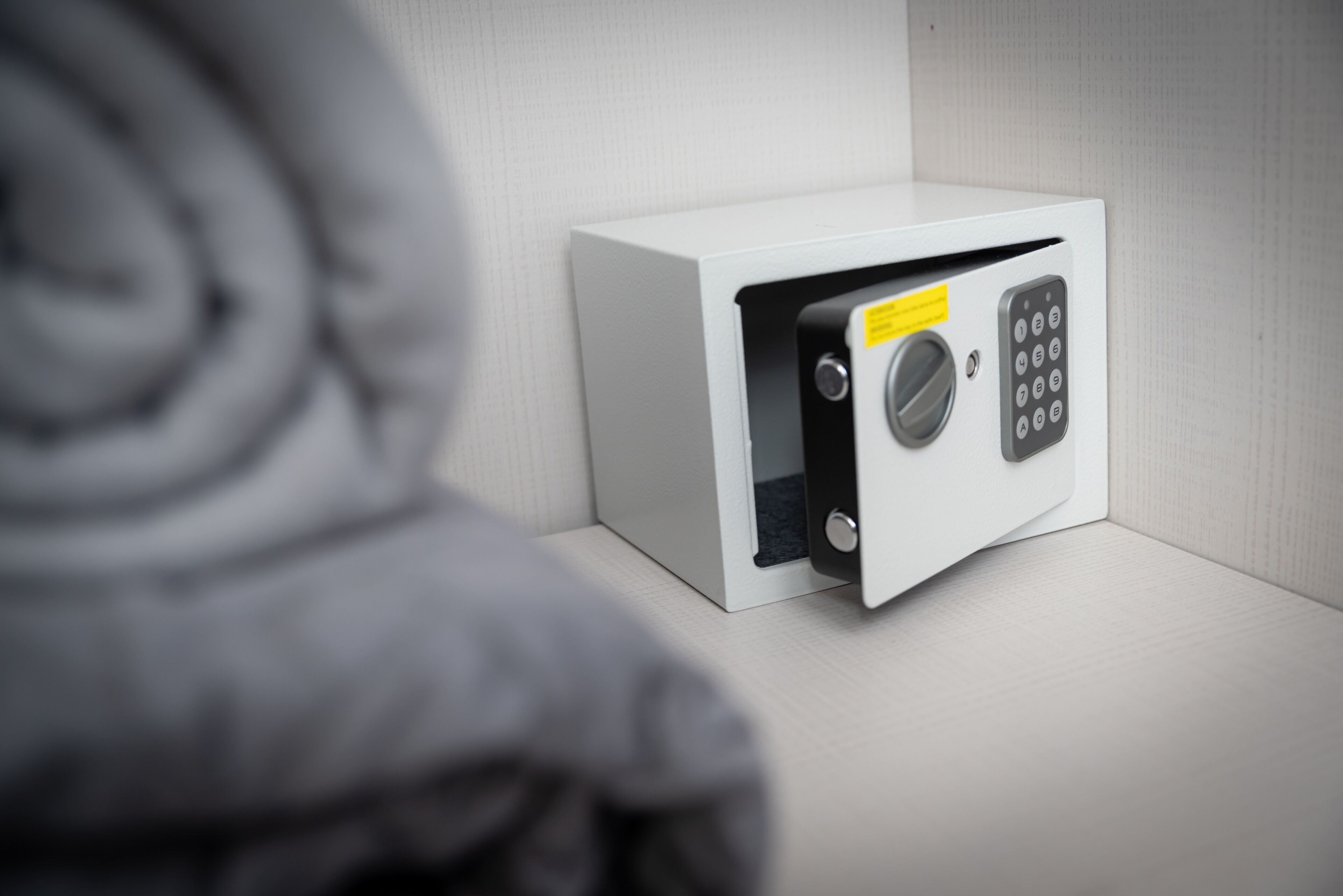 A white safe with a keypad and a yellow label, placed against a textured wall.