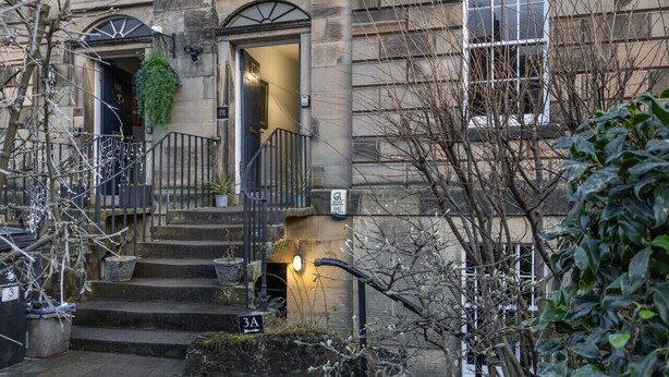 Un bâtiment doté d’une façade en pierre, d’un escalier menant à une porte et d’une enseigne indiquant l’entrée.