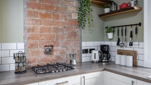 Une cuisine avec un mur en briques, une cuisinière à gaz, une machine à café et des ustensiles suspendus.