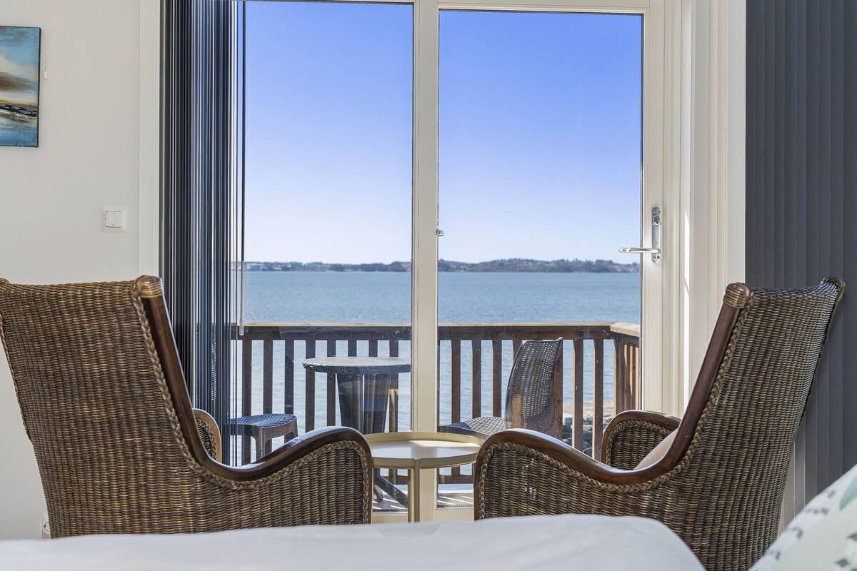 A balcony with wicker chairs, a small table, and a view of the water.
