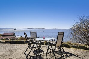A patio with a round table and four chairs, overlooking a body of water and a distant shoreline.