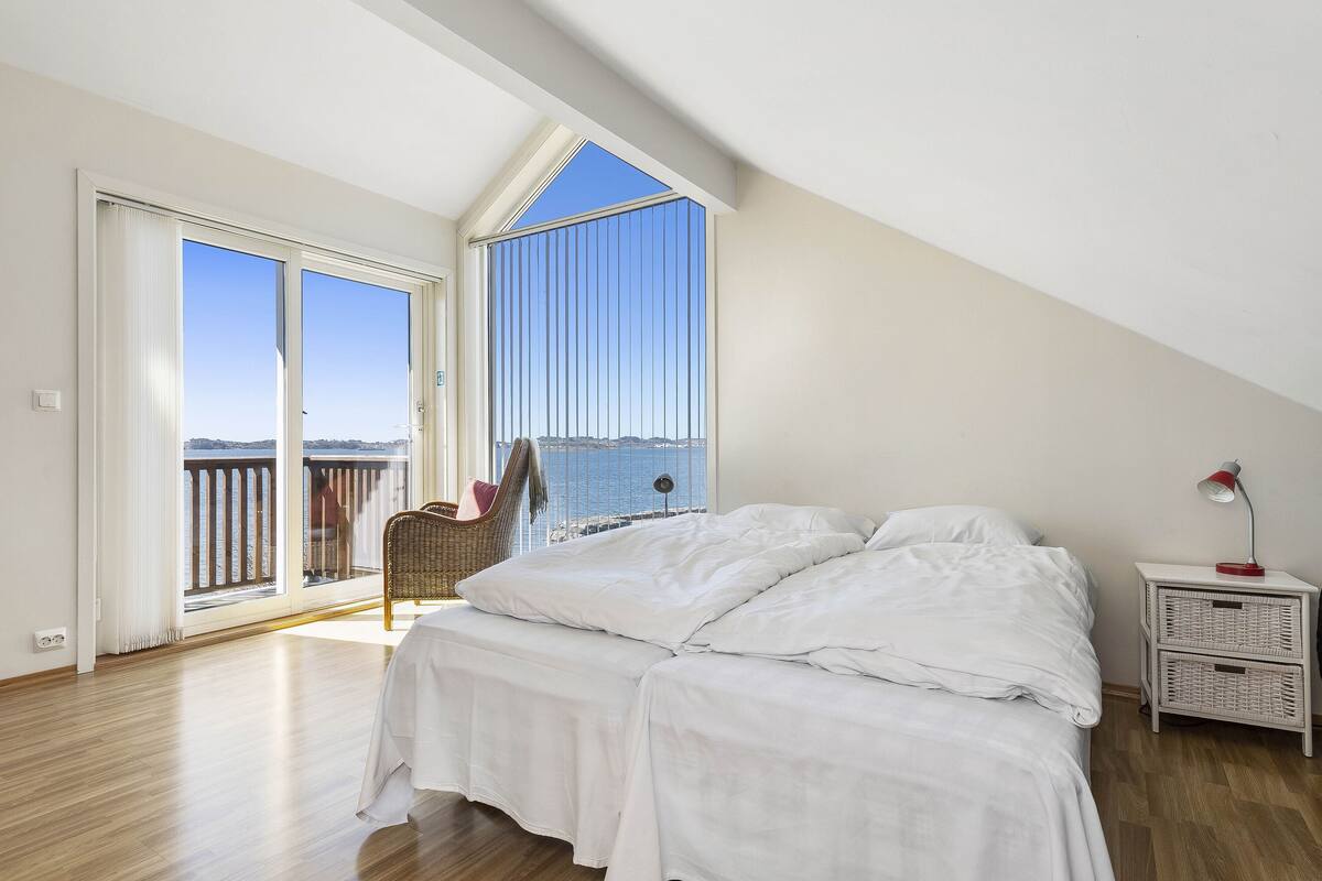 A bedroom with a large window, a bed, a nightstand, and a chair by the window.